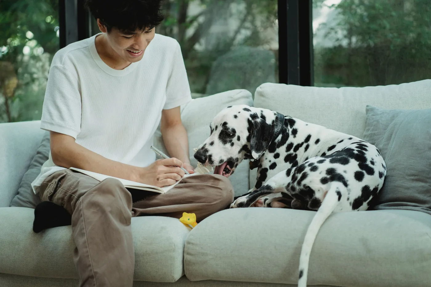 Una persona escribiendo en un cuaderno mientras su perro descansa a su lado